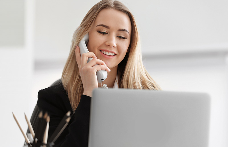 Mujer hablando por teléfono en la oficina y utilizando una laptop
