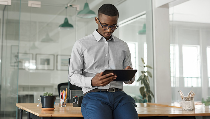 Home-Page-Mobile African American man leaning on desk and using tablet